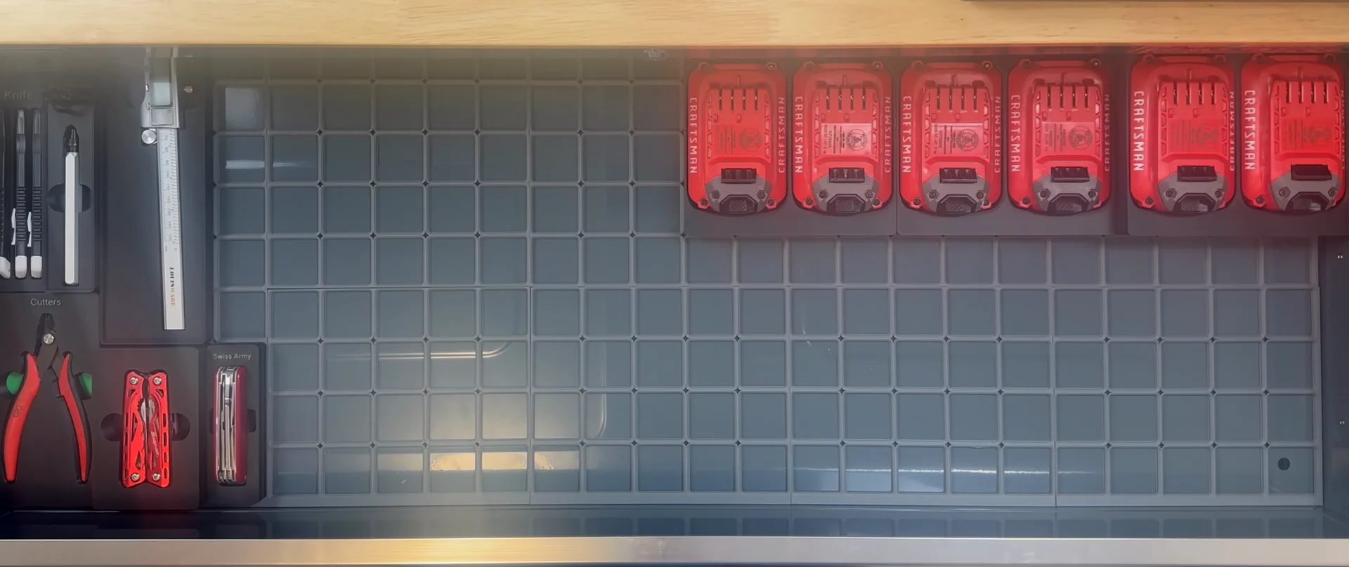 A drawer seen from above: a printed Gridfinity base, tool shadowboxes labeled Knife, Cutters and Swiss Army on the left, and six drill batteries in their shadowboxes along the back